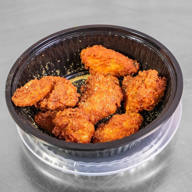 Seven crispy, breaded chicken wings in a black plastic takeout container on a metal surface.